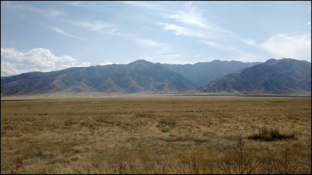 Photo of a large mountain range rising from a flat arid grassy plain